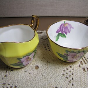 May include: A yellow creamer and sugar bowl set with a floral design. The creamer has a gold rim and a handle. The sugar bowl has a gold rim and a floral design on the side.