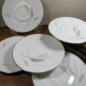 May include: Five white ceramic saucers with a silver rim and a delicate design of wheat stalks in shades of brown and green.