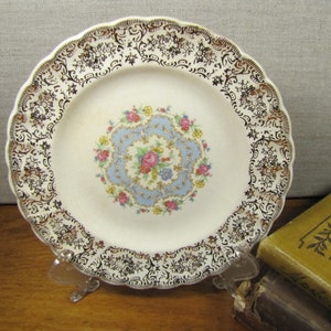 May include: A white ceramic plate with a blue and gold floral design. The plate has a scalloped edge and is decorated with a gold rim.