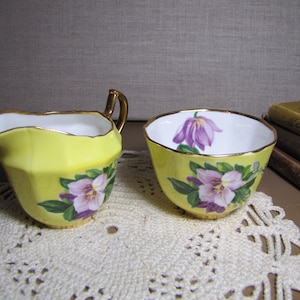 May include: A yellow creamer and sugar bowl set with floral designs. The creamer has a gold rim and a handle. The sugar bowl has a gold rim and a floral design on the side.
