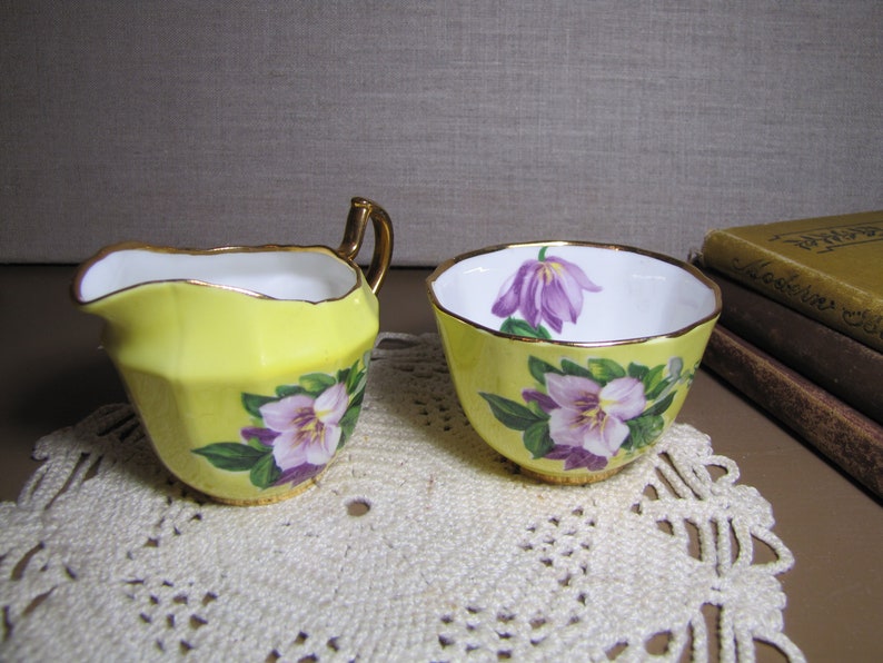 May include: A yellow creamer and sugar bowl set with floral designs. The creamer has a gold rim and a handle. The sugar bowl has a gold rim and a floral design on the side.