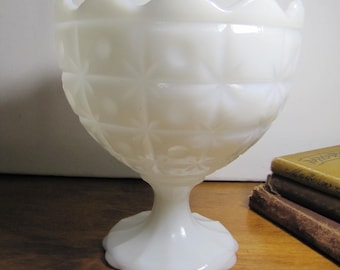 Op de afbeelding: Witte melkglas voetkom met een gegolfde rand en een geometrisch patroon. De kom staat op een houten oppervlak.