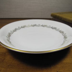 May include: A white ceramic bowl with a gold rim and a gray floral design around the edge.