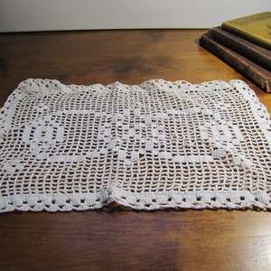 May include: White crocheted doily with a square design. The doily is made of delicate, intricate stitches and has a scalloped edge.