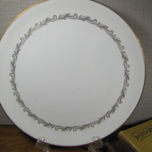 May include: A white ceramic plate with a gold rim and a silver leaf design around the edge.