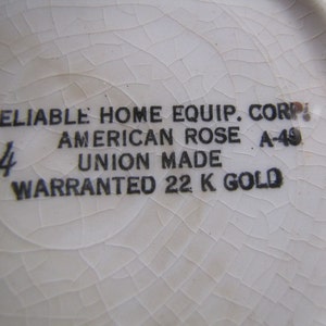 May include: Close-up of a white ceramic plate with black text that reads "RELIABLE HOME EQUIP. CORP. AMERICAN ROSE A-49 UNION MADE WARRANTED 22 K GOLD".