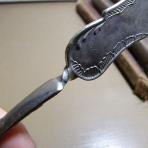 May include: A silver-colored, ornate, twisted metal bookmark with a decorative design on the top.