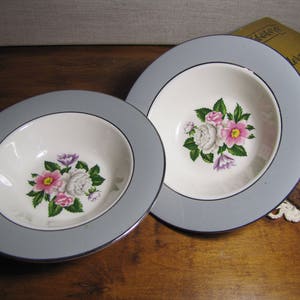 May include: Two gray and white floral patterned soup bowls with a silver rim. The bowls have a floral design with pink, white, and purple flowers.