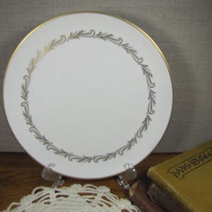 May include: A white ceramic plate with a gold rim and a delicate gold leaf design around the edge.