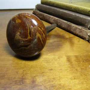 May include: A brown and tan ceramic door knob with a swirl pattern. The knob is attached to a metal rod.