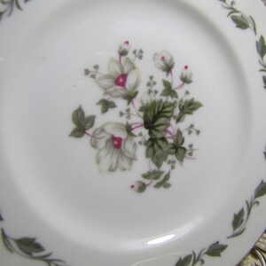 May include: White ceramic plate with a green floral design. The flowers are white with pink centers and green leaves.