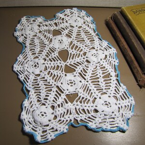 May include: White crocheted doily with a blue border. The doily has a delicate floral pattern.