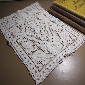 May include: A white crocheted doily with a delicate floral pattern. The doily is square shaped and has a fringed edge.