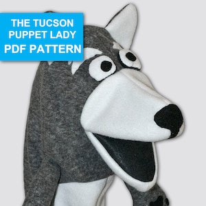 May include: Grey and white wolf puppet with black eyes, nose, and paw prints. The puppet has a large mouth that opens and closes. The text "THE TUCSON PUPPET LADY PDF PATTERN" is in a blue box at the top of the image.