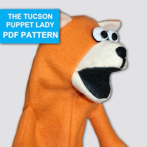 May include: Orange felt hand puppet with black eyes, a black mouth, and black paw prints on the arms. The puppet is titled "The Tucson Puppet Lady PDF Pattern".