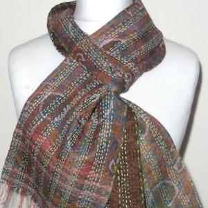 May include: A brown, pink, and blue patterned scarf with white stitching. The scarf is folded and draped around a white mannequin.