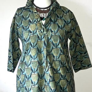 May include: A tunic-style top with a floral pattern in shades of green and blue. The top has a collared neckline and three-quarter sleeves. A beaded necklace is worn with the top. The garment is displayed on a white mannequin.