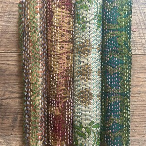 May include: Four rolled fabric quilts featuring intricate patterns and visible running stitch embroidery. The quilts display a variety of colours including brown, gold, cream, and dark green, with contrasting thread colours used for the stitching.