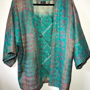 Könnte beinhalten: Türkis, rosa und grüne Patchwork-Kimono-Jacke mit V-Ausschnitt und Dreiviertelärmeln. Die Jacke hat ein Blumen- und geometrisches Muster und hängt an einem schwarzen Kleiderbügel.