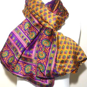 May include: A purple and gold silk scarf with a floral pattern. The scarf is folded and draped over a white mannequin.