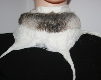 May include: A white felted wool neck warmer with a band of gray and brown fur around the neck. The neck warmer has long, pointed extensions that drape down the front. The garment is worn over a black top.