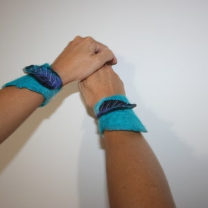 May include: Two turquoise blue felt wrist cuffs with black and purple felt leaf embellishments.