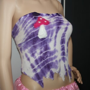 May include: A strapless top with a tie-dye pattern in shades of purple and white. The top features a felt mushroom appliqué with a red cap and white stem.