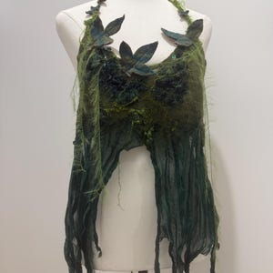 Peut inclure: Un haut à encolure américaine dans des tons de vert foncé et forêt, doté d'un corsage texturé et feutré orné de feuilles en tissu en trois dimensions et d'ornements sombres. L'ourlet se compose de longues bandes de tissu effilochées.