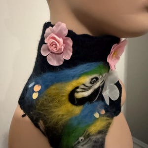 Puede incluir: Un calentador de cuello de fieltro negro con un diseño de loro colorido, flores rosas y lentejuelas.