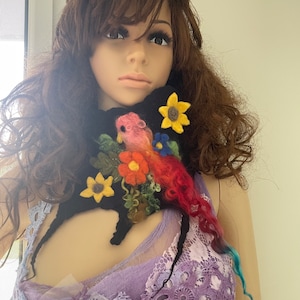 May include: A black felt neck warmer with a colorful embroidered bird and flowers. The flowers are yellow, red, pink, and blue.