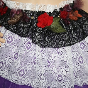 Könnte beinhalten: Ein lila-weißer Tüllrock mit schwarzer Spitzenborte und floralen Verzierungen.
