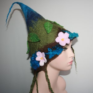 May include: A green, blue, and brown felt hat with a long, pointed crown. The hat is decorated with felt flowers and leaves.