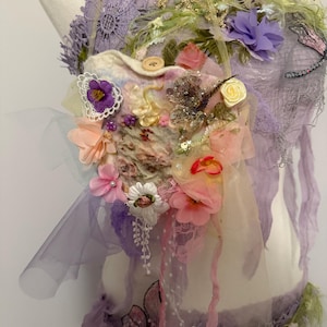 Op de afbeelding: Een delicaat, handgemaakt, paars en wit kant topje met een vilt hartje versierd met bloemen, vlinders en kralen. Het topje is perfect voor een grillige, feeërieke look.