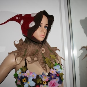 May include: A whimsical costume featuring a red and white polka-dotted hood with a long, pointed tip. The ensemble includes a brown, leaf-like collar and a floral bodice, creating a fairy or woodland creature theme.