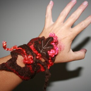 May include: A brown and pink crocheted bracelet with a leaf design. The bracelet is made with a variety of yarns and textures.