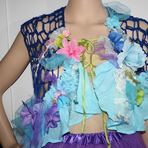 May include: A blue crochet top with a floral design. The top is decorated with blue, pink and white flowers, as well as green leaves. The top is tied at the front with a green ribbon.
