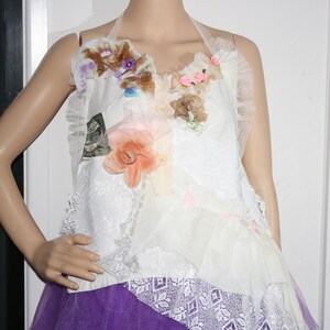 May include: A white halter top with a layered design featuring lace, tulle, and fabric flowers in shades of pink, brown, and purple. The top is accented with a small pink bow.