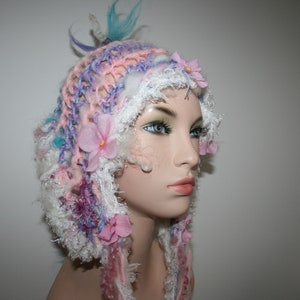May include: A pink, white, and blue crocheted hat with flower embellishments. The hat is made with a variety of textures and colors, including fluffy yarn, lace, and crocheted flowers.