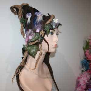 May include: A brown felt hat with a whimsical design featuring ivy leaves, mushrooms, and flowers. The hat is worn on a mannequin with a white face.