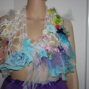 May include: A white crocheted top with blue, pink and green fabric flowers. The top is decorated with lace and tulle.