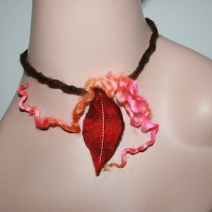 May include: A brown yarn necklace with a red felt leaf pendant and pink and orange yarn accents.