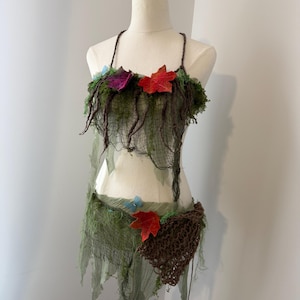 Könnte beinhalten: Zweiteiliges Kostüm auf einer Schaufensterpuppe. Das Oberteil ist ein Neckholder-Stil mit einem Moos- und Netzdesign, verziert mit roten und lila Blattakzenten. Das Unterteil ist ein Rock mit passendem Netz- und Blattdesign.