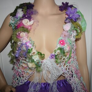 May include: A crocheted vest featuring a floral design. The vest is made in a variety of colours, including pink, green, white, and purple. The vest is decorated with crocheted flowers and leaves.