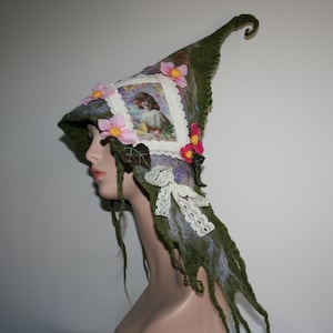 May include: A green felt witch hat with a pointed crown and a long, flowing tail. The hat is decorated with pink and white flowers, a small picture of a girl, and white lace.