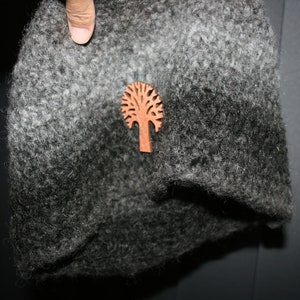 May include: A grey and black fuzzy hat with a wooden tree-shaped pin.