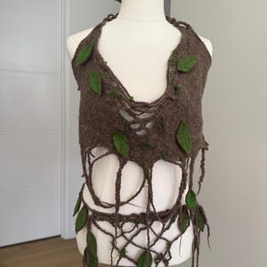 May include: A brown felted halter top featuring a deep neckline and an open, web-like fringe hem. The garment is decorated with several small, flat green fabric leaves and small patches of green moss-like texture attached to the brown felt surface.