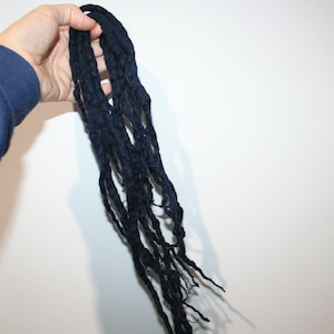 May include: A long strand of dark blue yarn, resembling dreadlocks, is held in a hand.