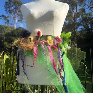 Pode incluir: Saia artesanal num manequim, com cós em feltro com detalhes de lã colorida em rosa, roxo e amarelo. Uma saia de tule verde pende por baixo, com detalhes azuis e roxos. O design incorpora um ninho de pássaro. Medidas em cm.