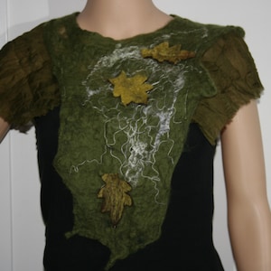 Puede incluir: Un collar de tela de fieltro verde con adornos de hojas blancas y amarillas. El collar se lleva sobre una camisa negra.