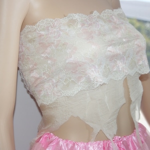 May include: A white lace top with pink accents. The top is strapless and has a ruffled hem. The top is made of a sheer fabric and is very delicate.